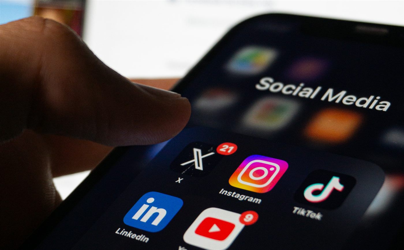 Mano tocando la carpeta de redes sociales en un celular, con una pantalla de acceso a una web de fondo