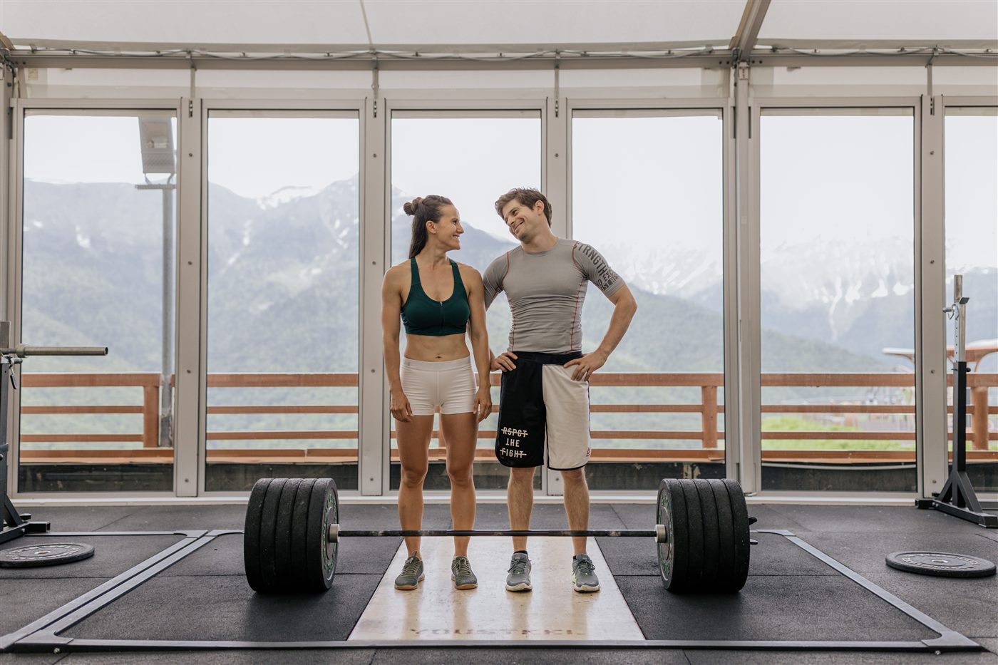Pareja entrenando con pesas en gimnasio luminoso con vista a las montañas